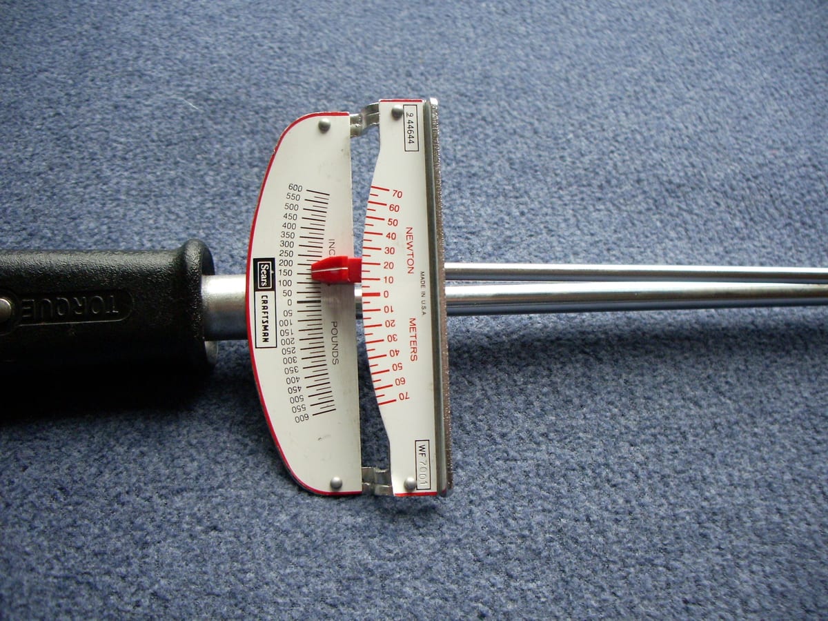 Close-up of a Craftsman beam torque wrench scale, graduated in inch-pounds from 0 to 600 in both directions with a Newton-metre scale alongside, the red pointer resting at zero